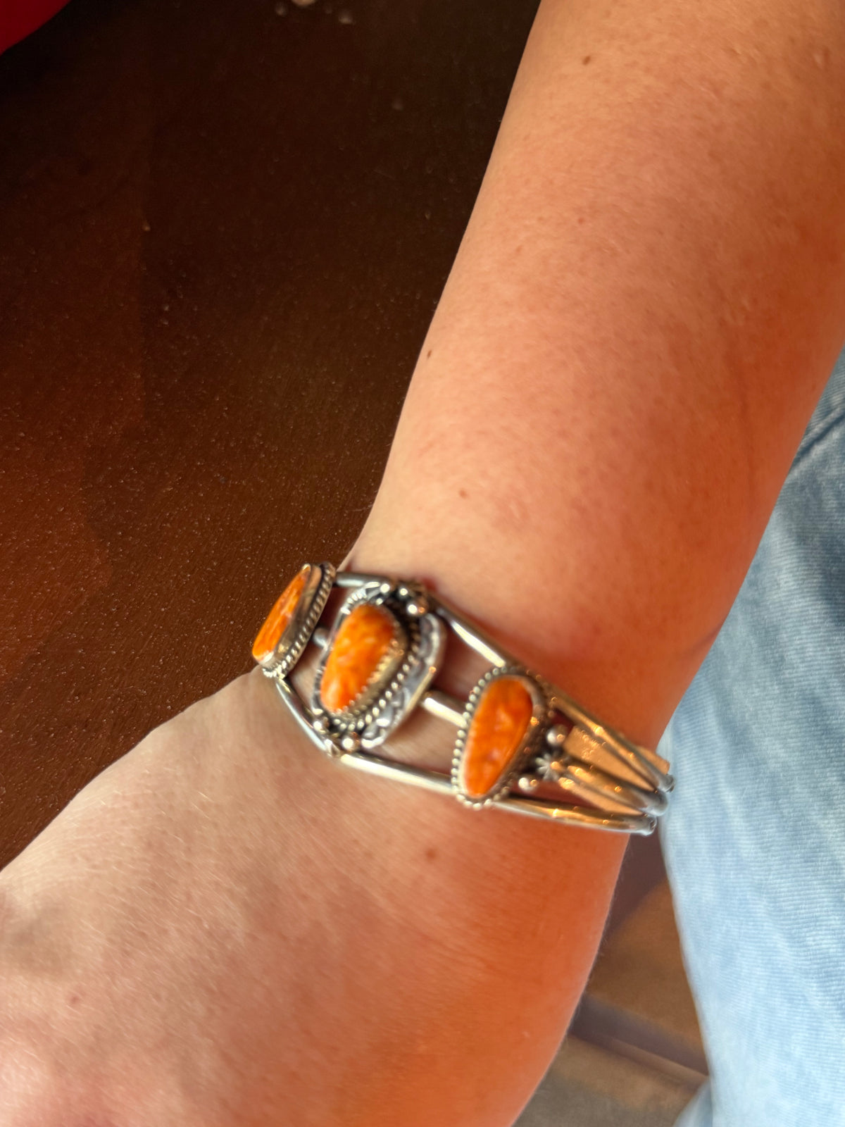 A close-up of a person's wrist wearing a silver cuff bracelet with three oval orange stones and silver-toned metal detailing.