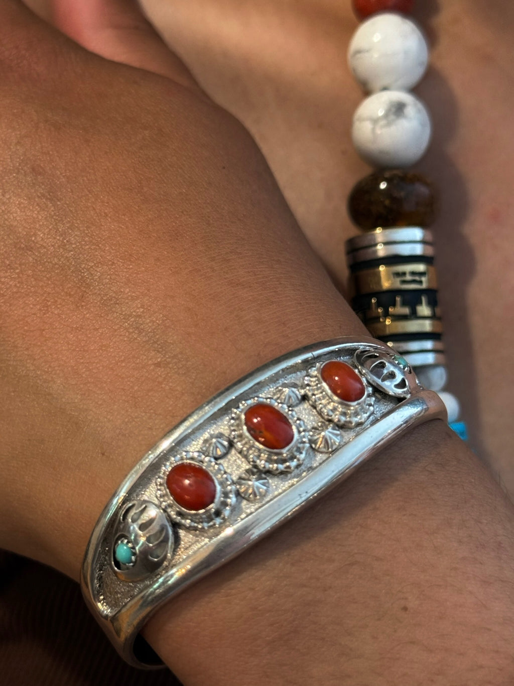 A close-up of a silver-toned cuff bracelet with four oval red cabochon stones and small turquoise accents, worn on a person's wrist.