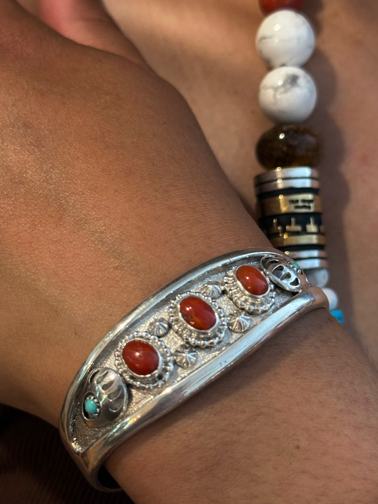 A close-up of a silver-toned cuff bracelet with four oval red cabochon stones and small turquoise accents, worn on a person's wrist.