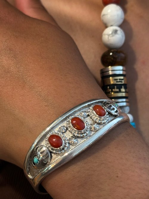 A close-up of a silver-toned cuff bracelet with four oval red cabochon stones and small turquoise accents, worn on a person's wrist.