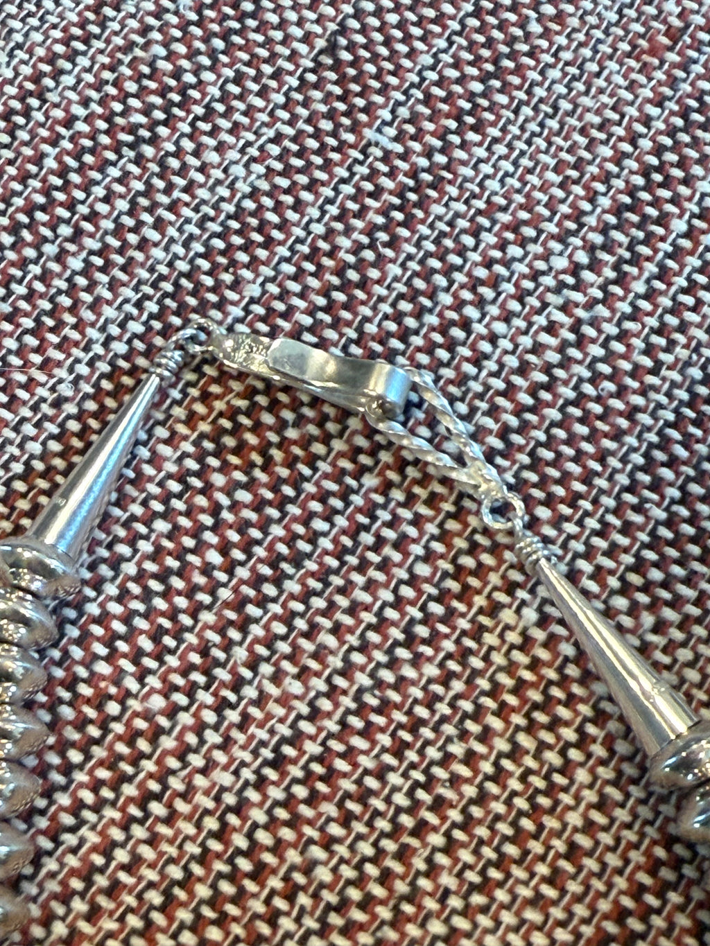 A close-up of a silver-toned bracelet or chain accessory laid on a woven brown, beige, and white textile surface.