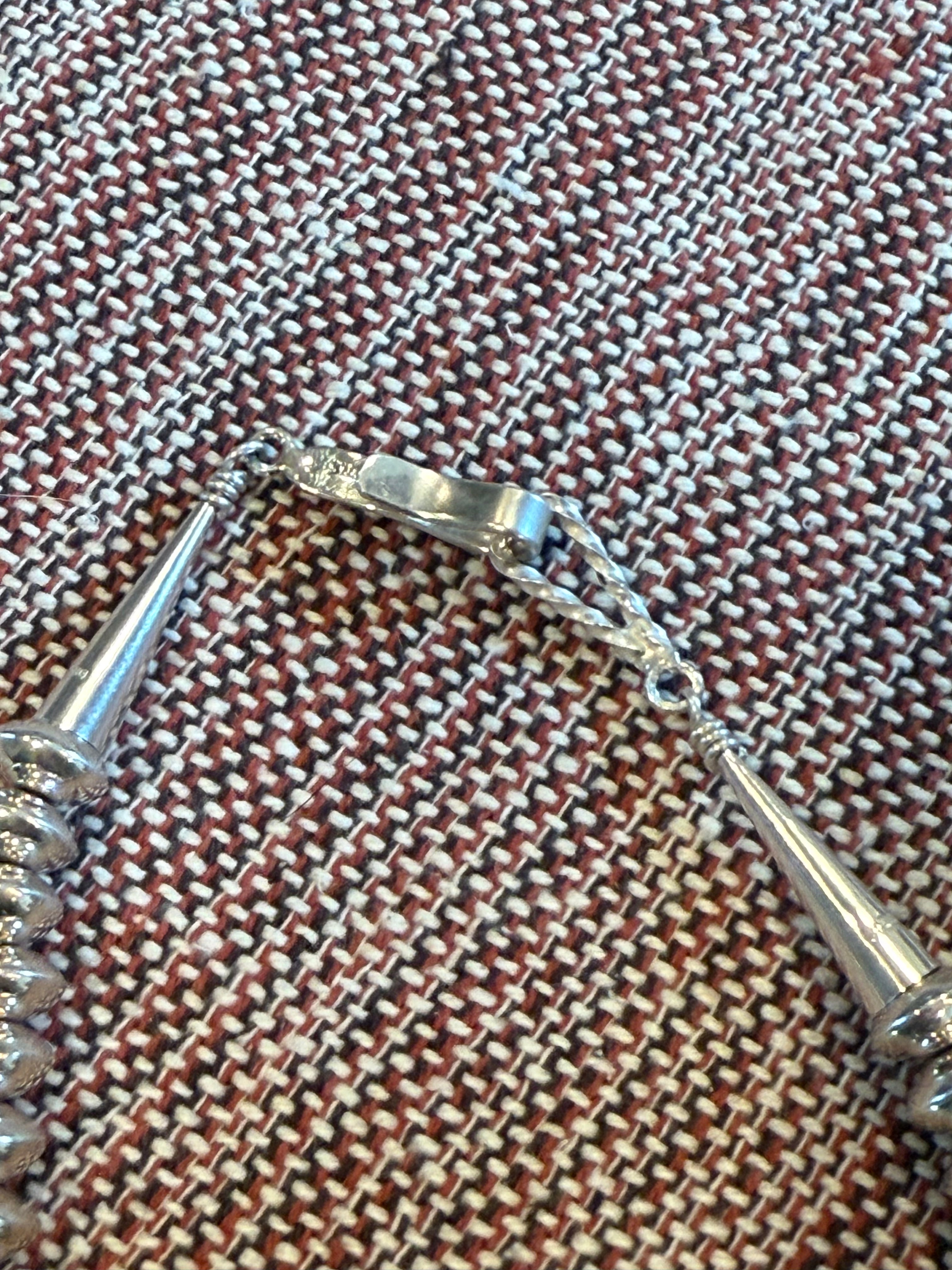 A close-up of a silver-toned bracelet or chain accessory laid on a woven brown, beige, and white textile surface.