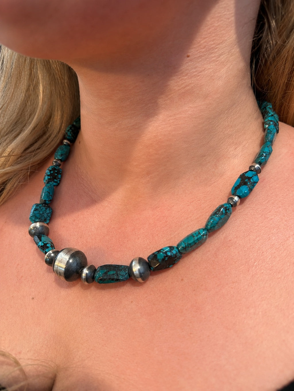 A close-up of a person's neck and collarbone wearing a turquoise and silver beaded necklace.