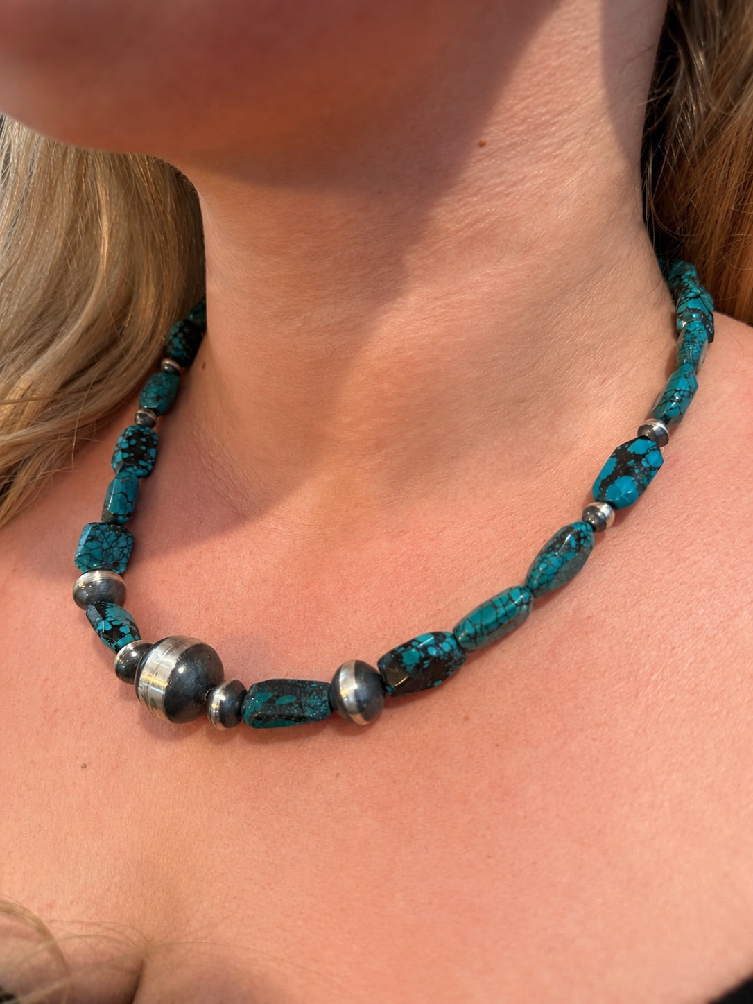 A close-up of a person's neck and collarbone wearing a turquoise and silver beaded necklace.