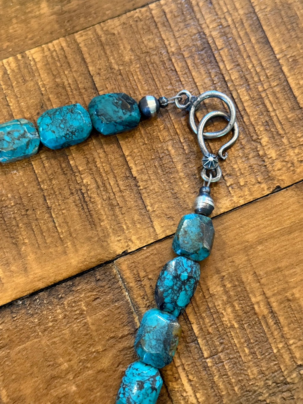Turquoise stone beads with a silver toggle clasp, laid on a rustic wooden surface.