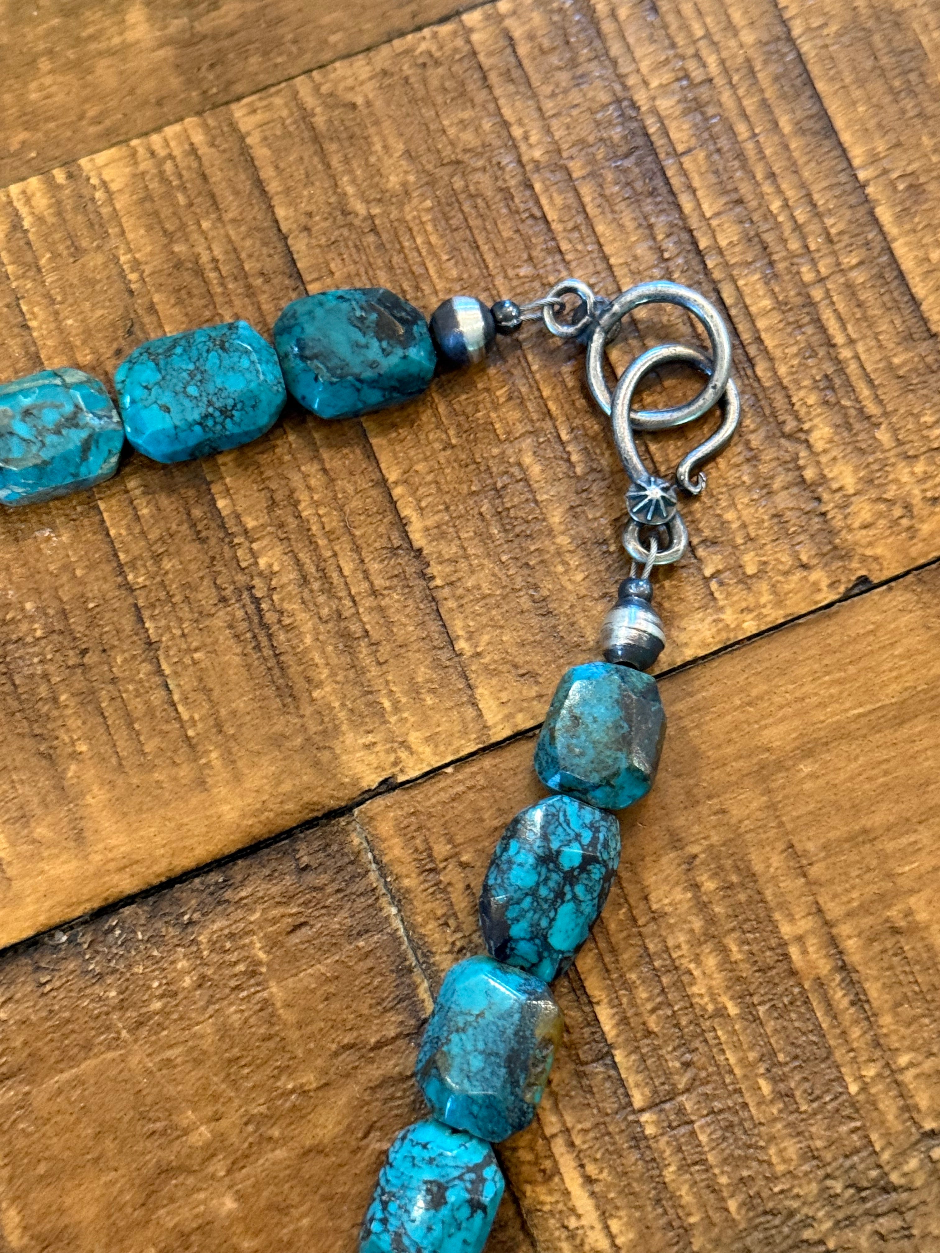 Turquoise stone beads with a silver toggle clasp, laid on a rustic wooden surface.
