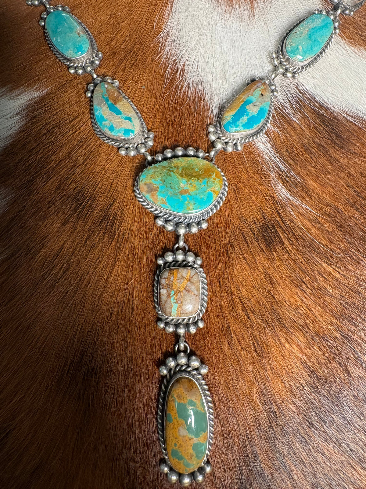 A silver-toned necklace with multiple turquoise and orange marbled stones, laid flat on a brown and white fur surface.