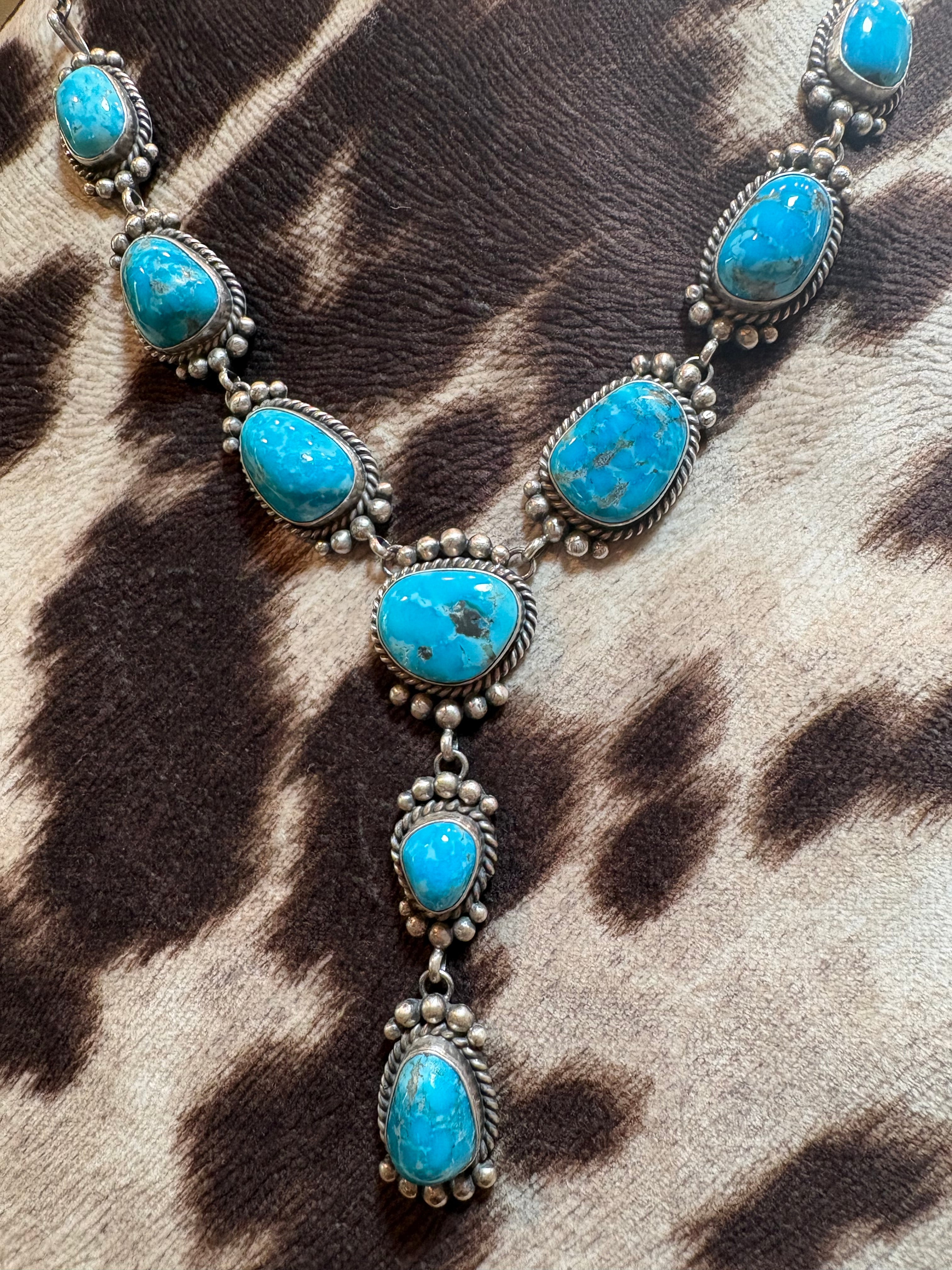 A silver-toned necklace featuring multiple oval turquoise stones set in ornate silver bezels, displayed on a brown and beige animal-print fur surface.