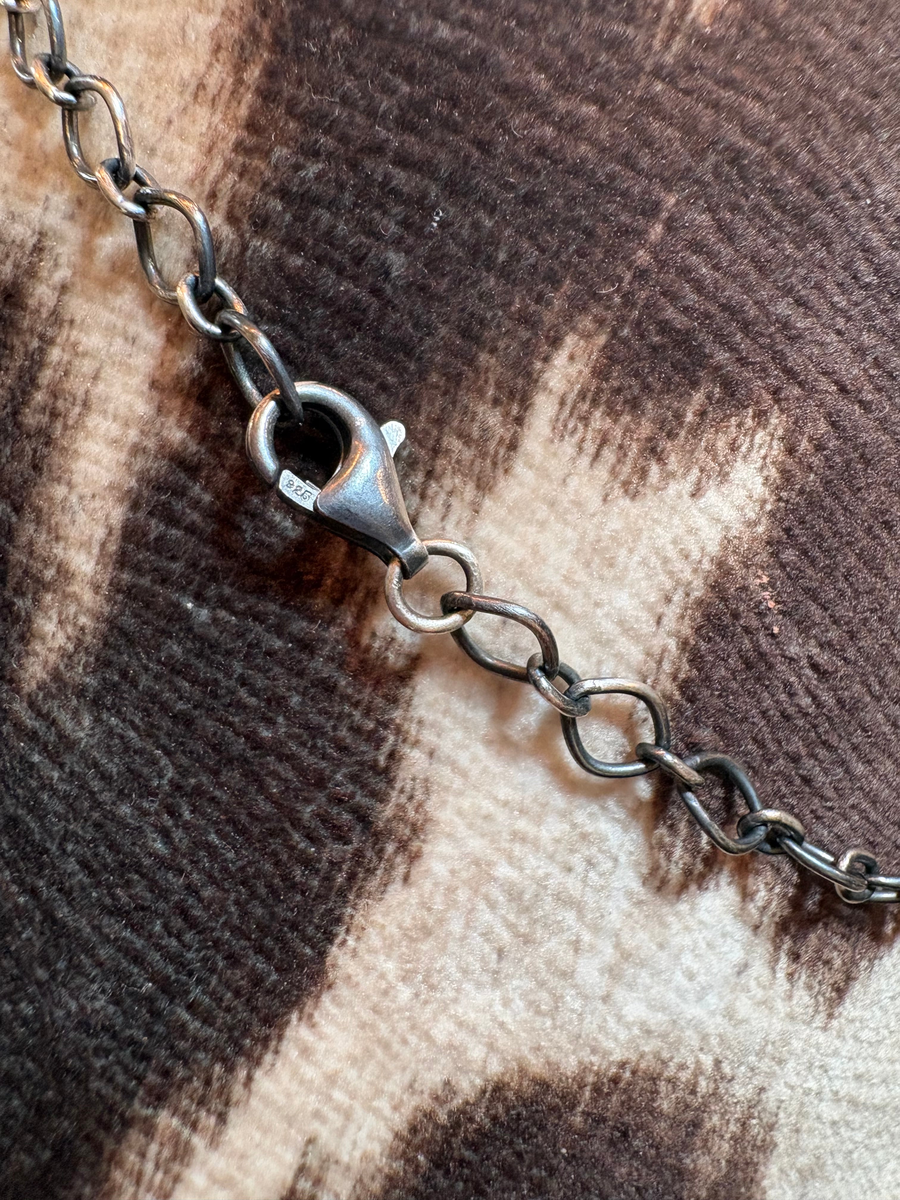 A close-up of a dark gunmetal chain with a lobster clasp, resting on a brown and beige patterned fabric background.