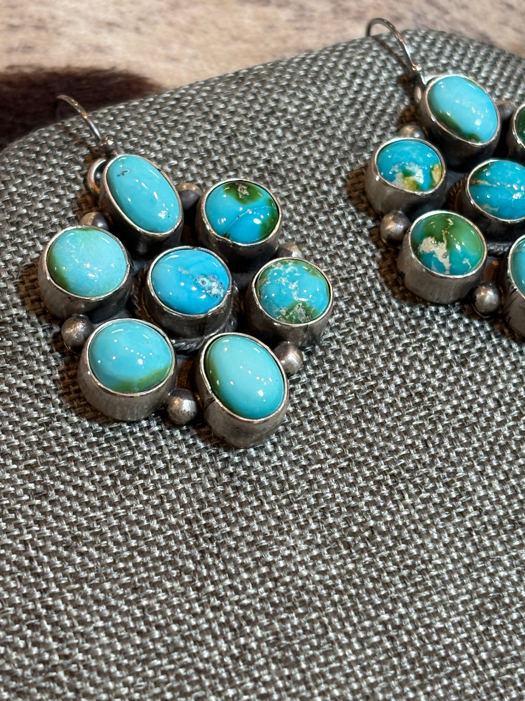 A pair of silver-toned dangle earrings with multiple oval turquoise-blue stones, displayed on a textured gray woven fabric surface.