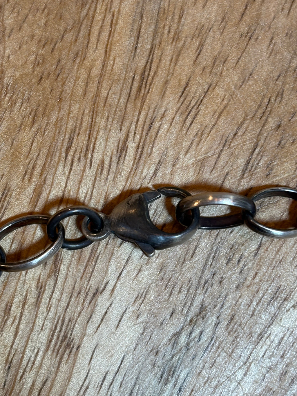 A close-up of a dark metal link chain bracelet or necklace clasp resting on a brown wood-grain surface.