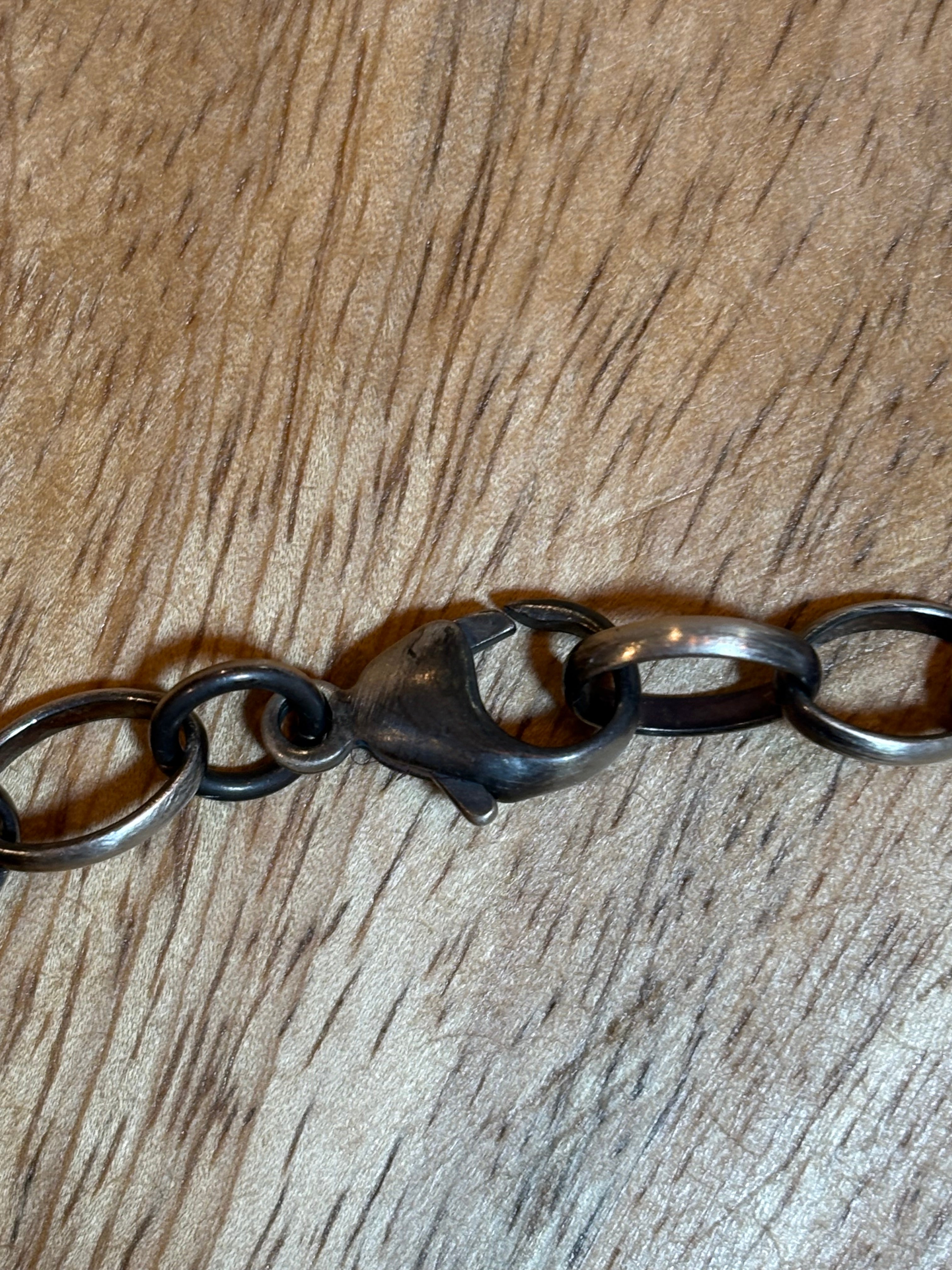 A close-up of a dark metal link chain bracelet or necklace clasp resting on a brown wood-grain surface.