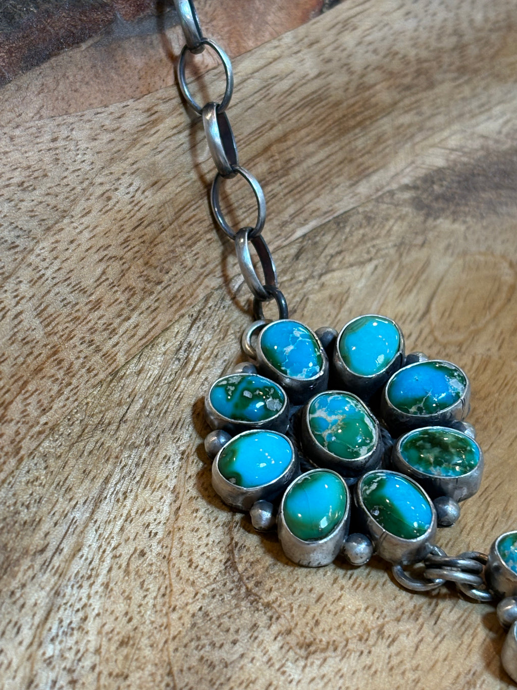 A close-up of a silver-toned necklace with a cluster pendant featuring multiple oval turquoise stones, resting on a wooden surface.