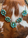 A silver-toned statement necklace featuring multiple clusters of turquoise stones, displayed on a brown and white cowhide background.