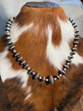 A beaded necklace displayed on a cowhide mannequin. The necklace features large polished dark gray stone beads and smaller pink accent beads.
