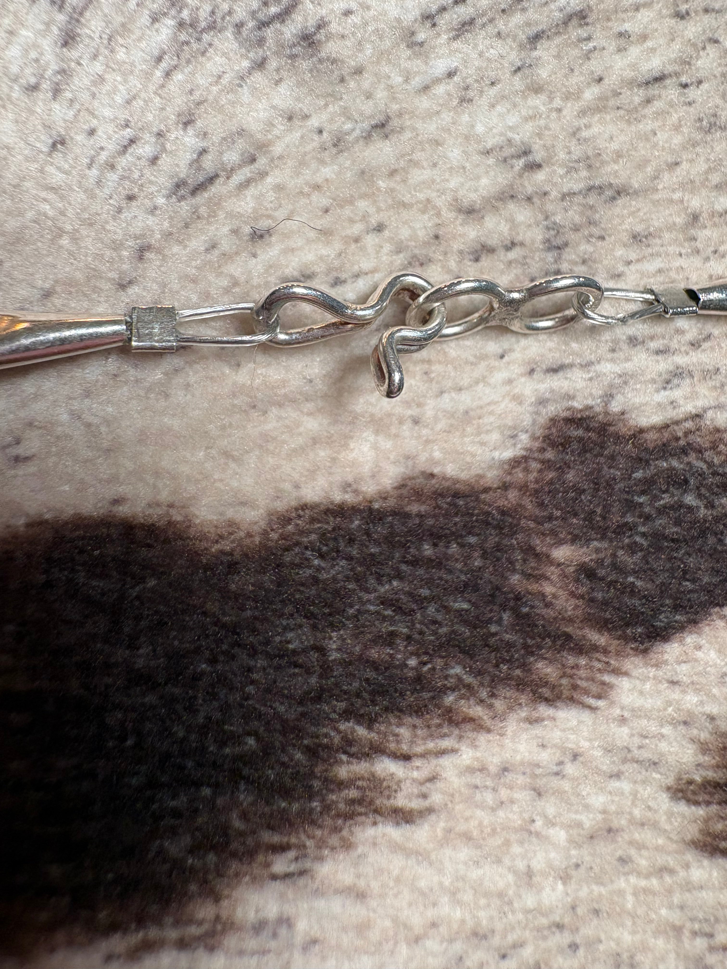 Close-up of a silver-toned metal chain bracelet or necklace clasp resting on a textured cowhide surface with dark brown and cream patches.