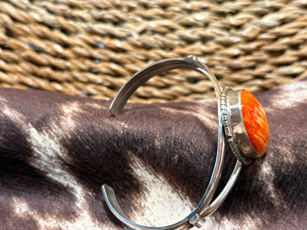 A sterling silver cuff bracelet with a carved orange cabochon stone, resting on a brown and white zebra-patterned hide with a woven straw background.