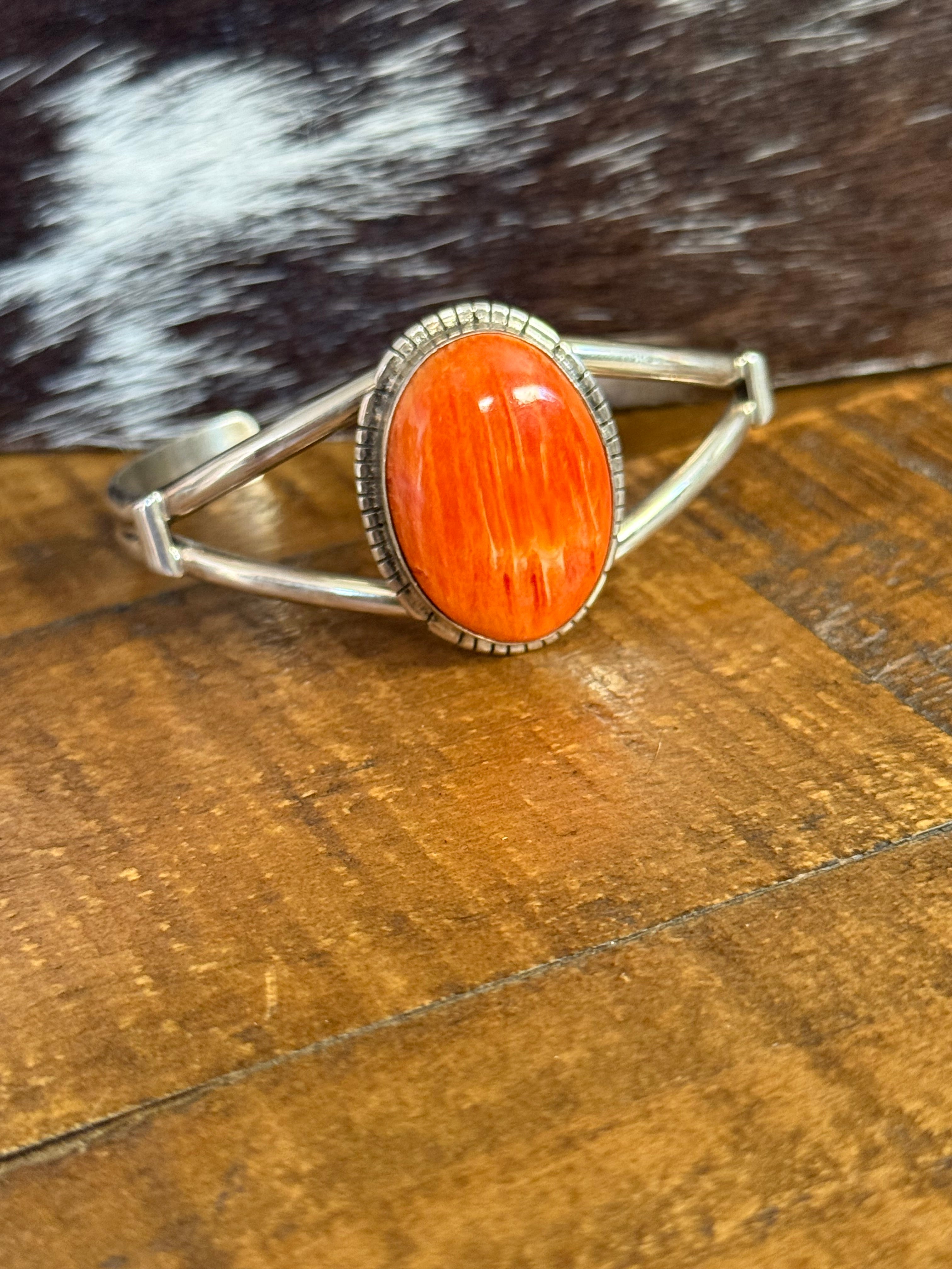A silver-toned wrap-style cuff with a large oval orange stone, photographed on a wooden surface next to a black-and-white fur texture.
