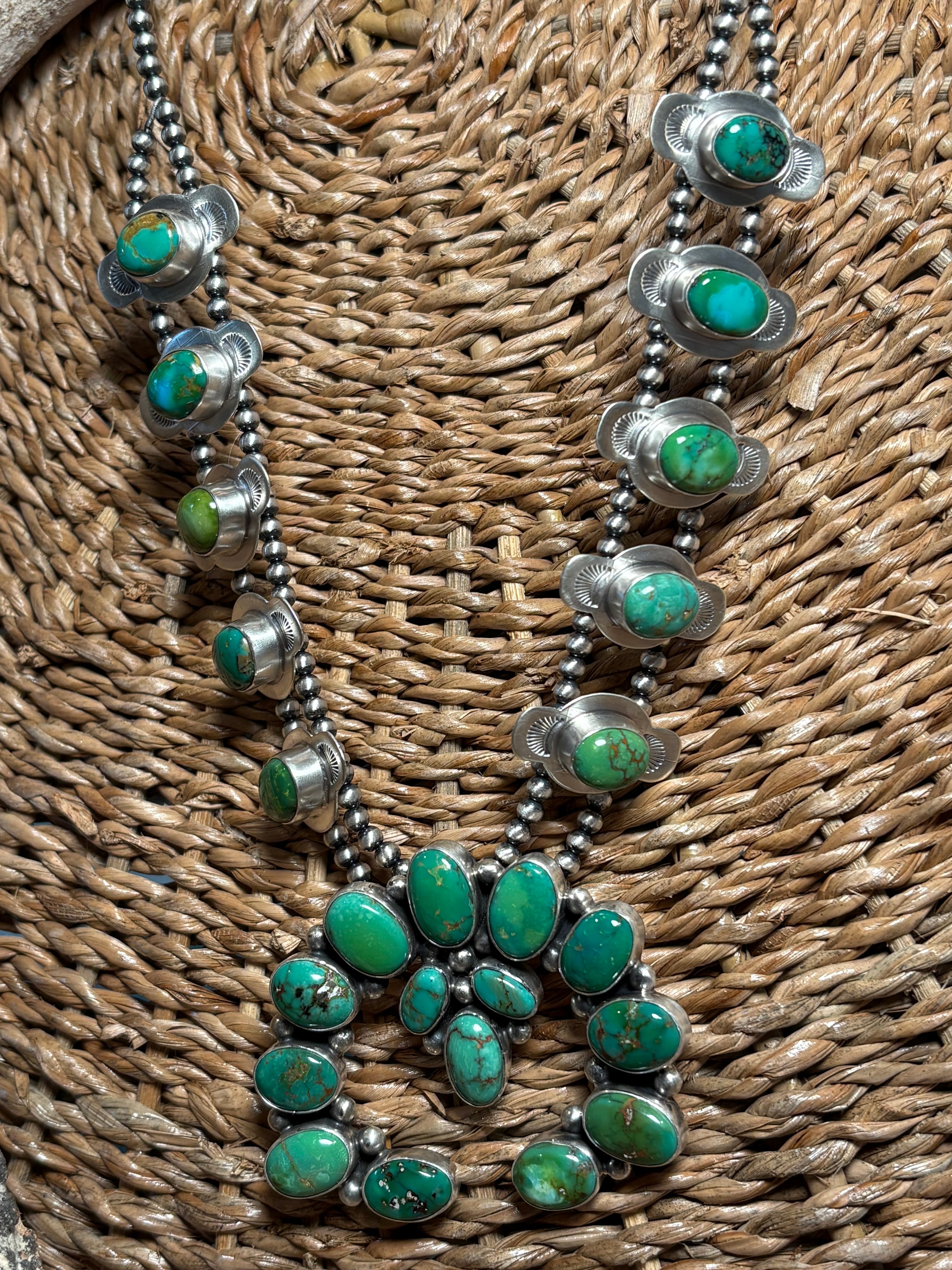 A silver-toned multi-strand necklace featuring vibrant green turquoise stones, displayed on a woven brown wicker surface.