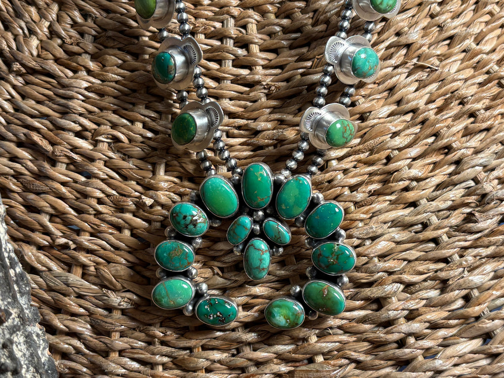 A Southwestern-style turquoise necklace with oval green turquoise stones set in silver, displayed on a woven brown wicker surface.